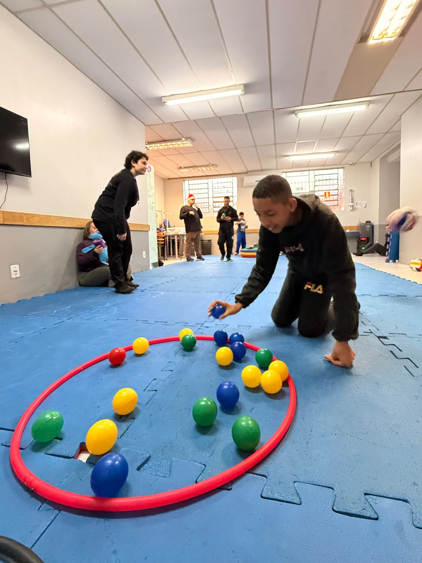 Educador organiza bolinhas coloridas dentro de um bambolê, no tatame da sala.