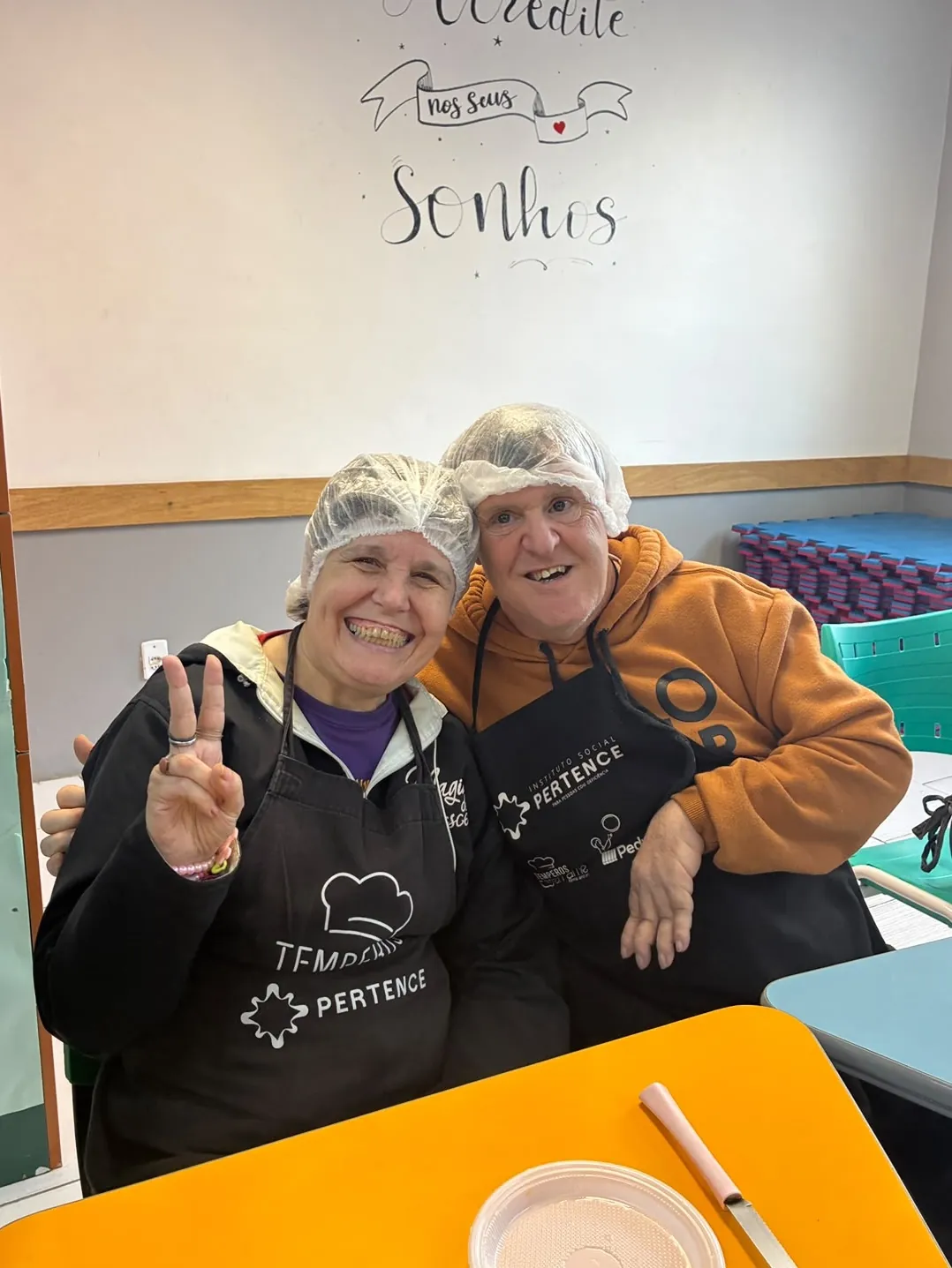 Dupla de touca e avental da oficina de culinária faz sinal de positivo.