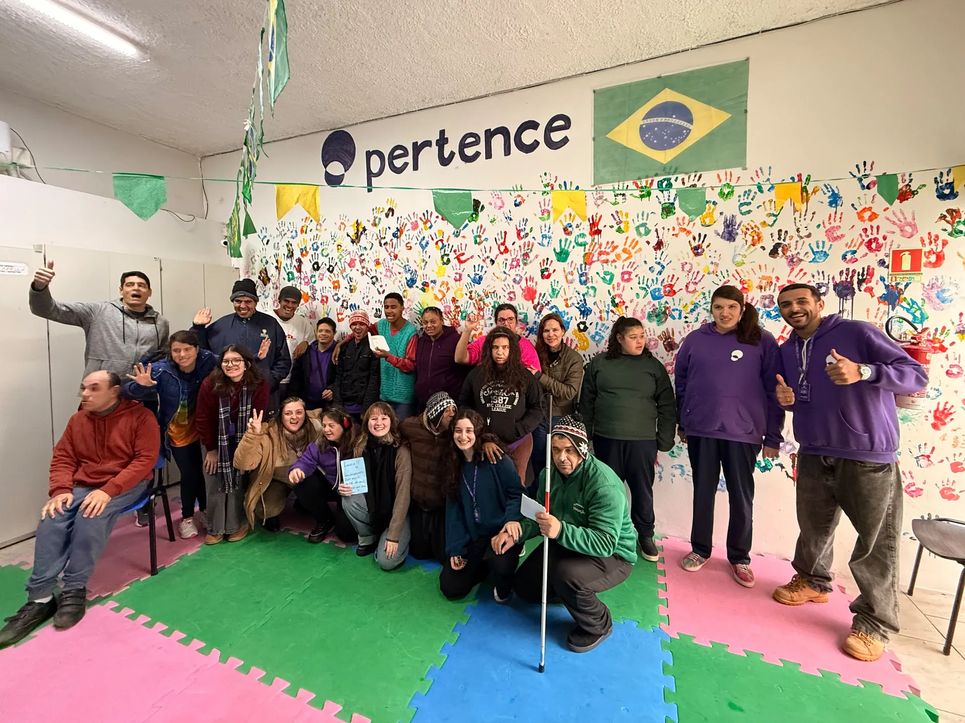 Turma reunida diante do mural de mãos pintadas da sede do Pertence.