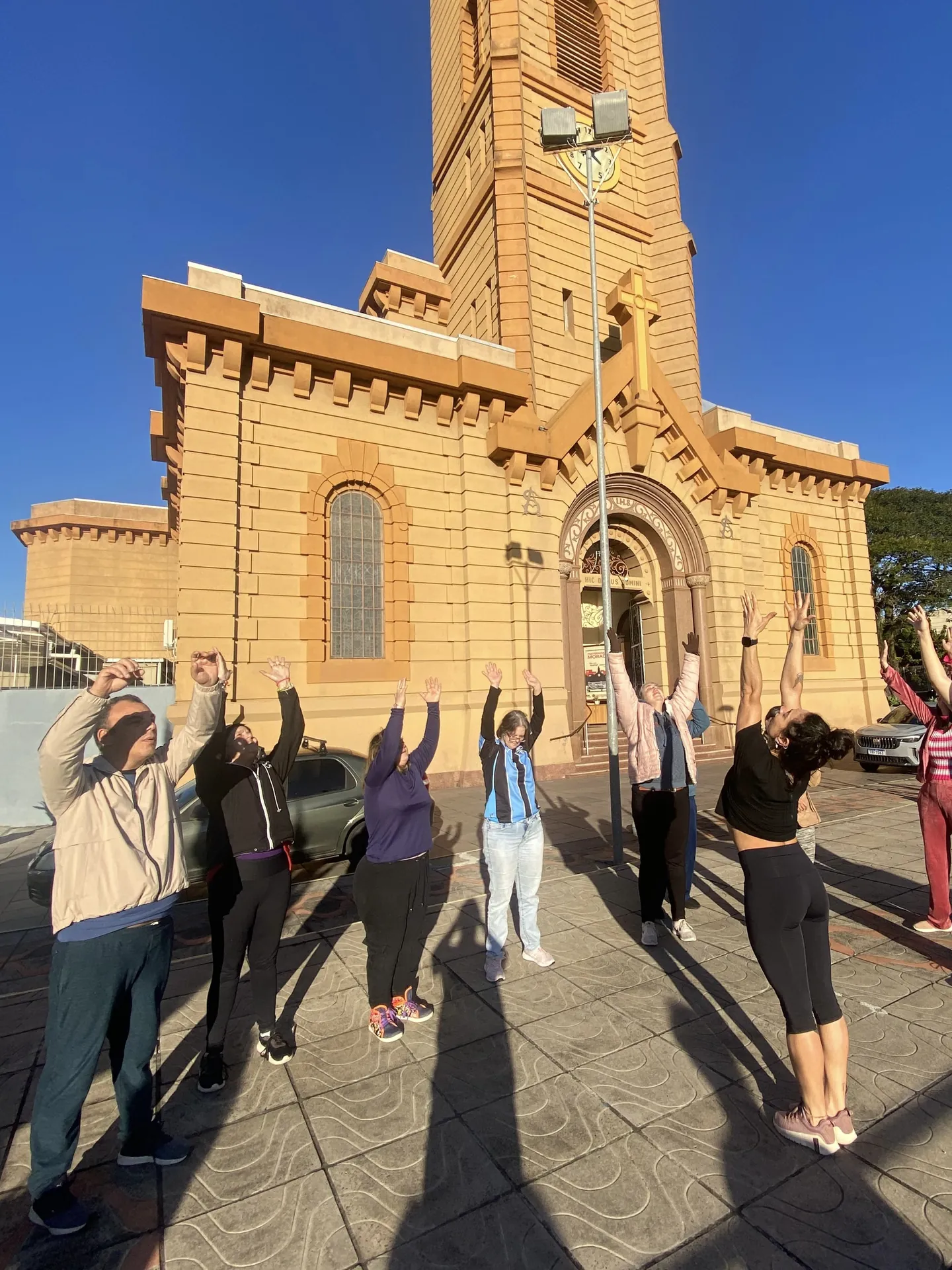 Grupo de braços erguidos em frente a uma igreja, em saída da oficina.