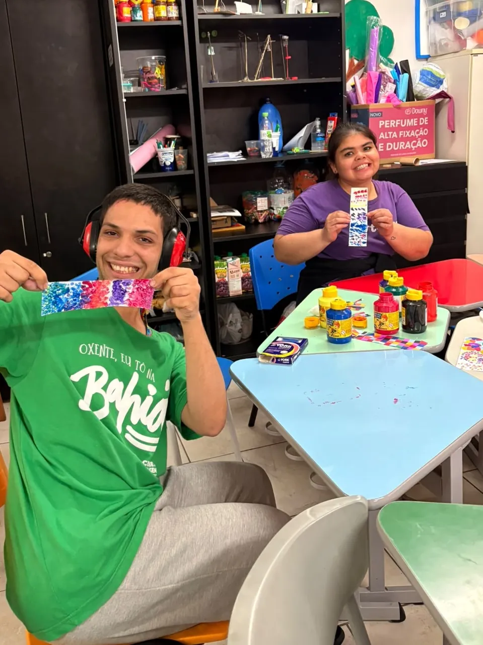 Dois participantes mostram os trabalhos coloridos que fizeram na oficina de artes.