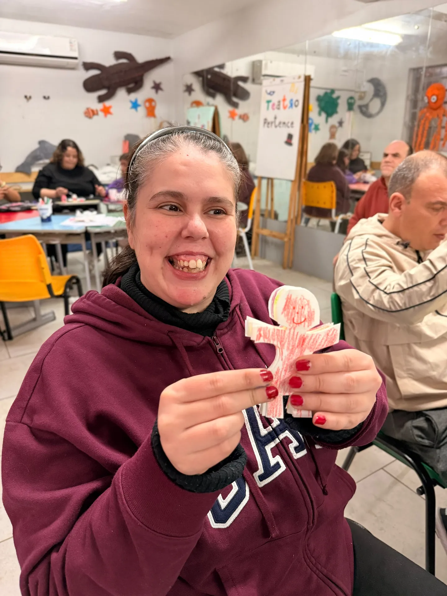 Participante da oficina de artes mostra um boneco de papel que acabou de recortar.