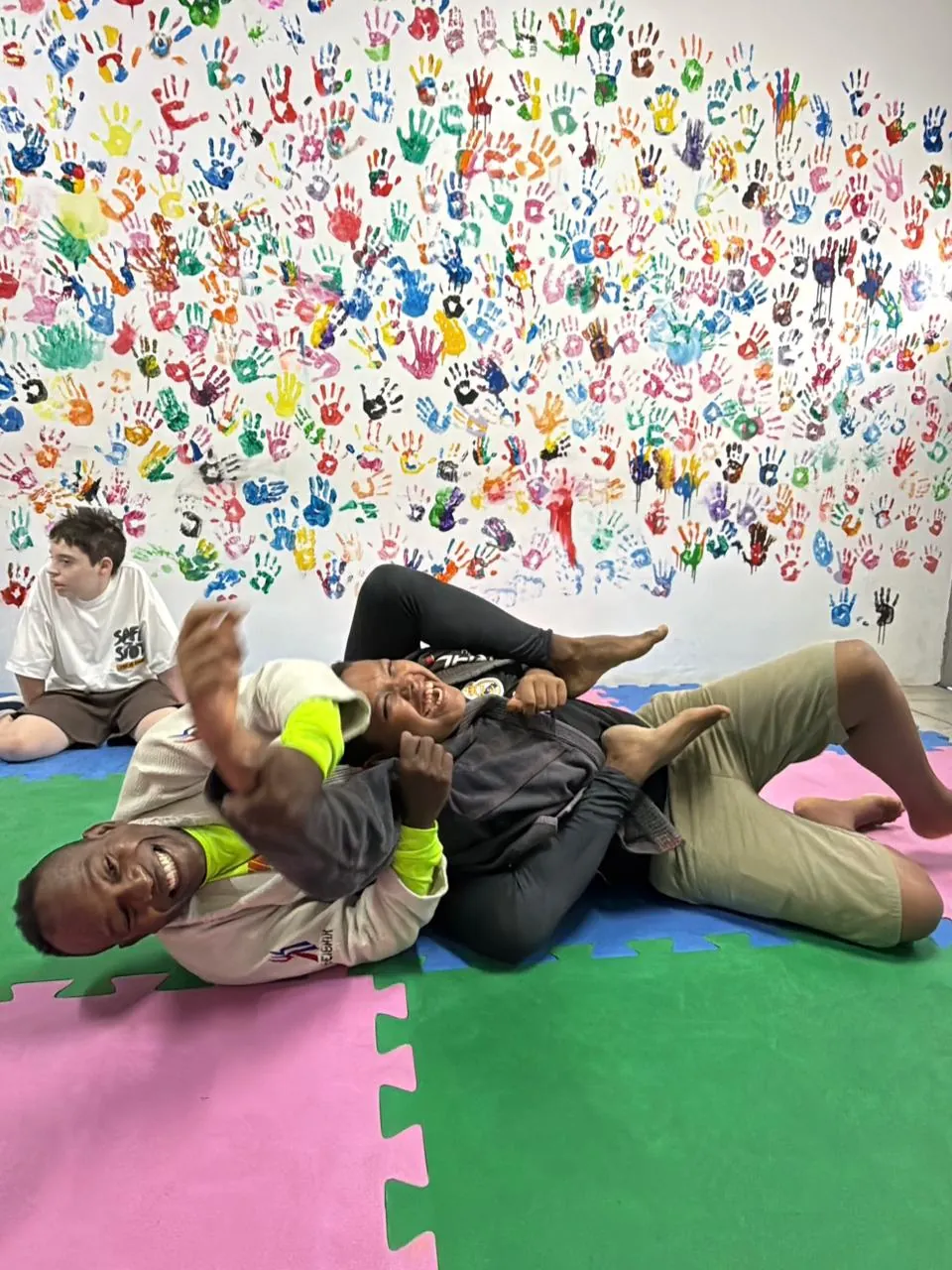 Dupla treina jiu-jitsu no tatame, sorrindo durante o exercício.