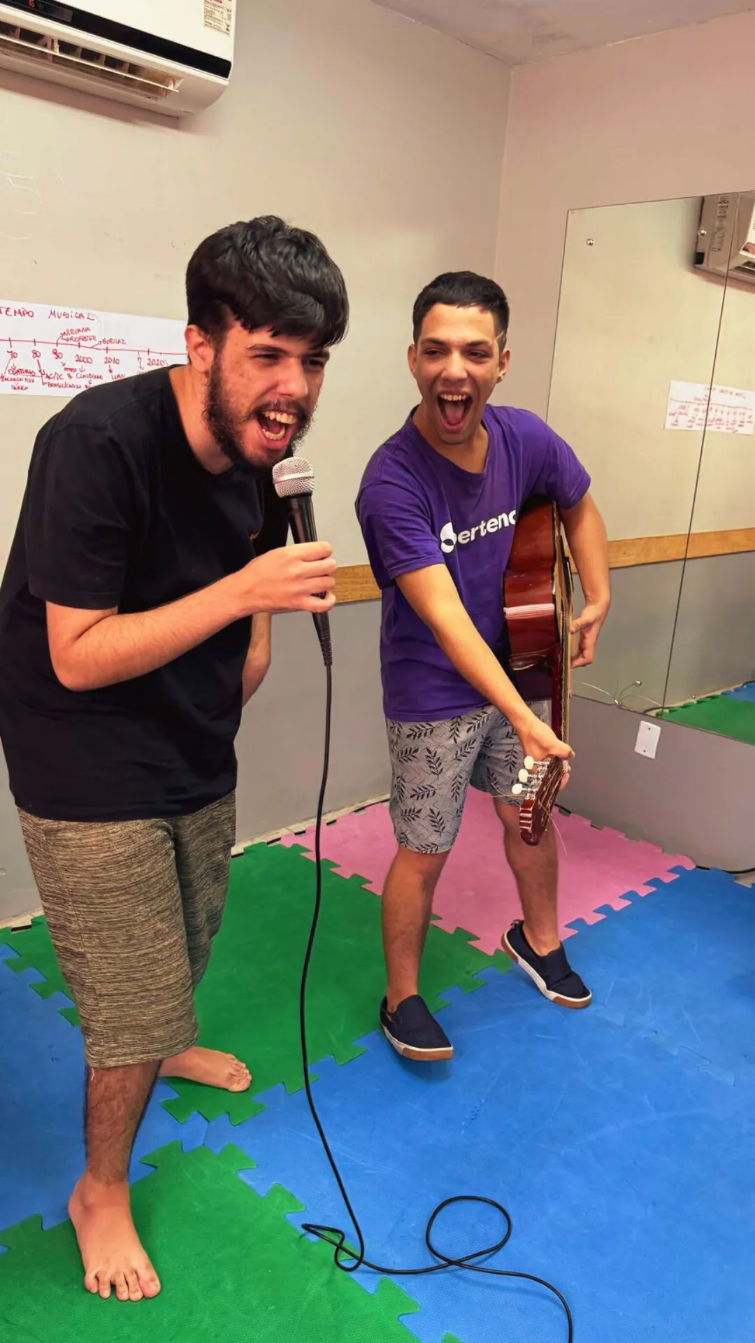 Dupla canta ao microfone e toca violão na oficina de música.