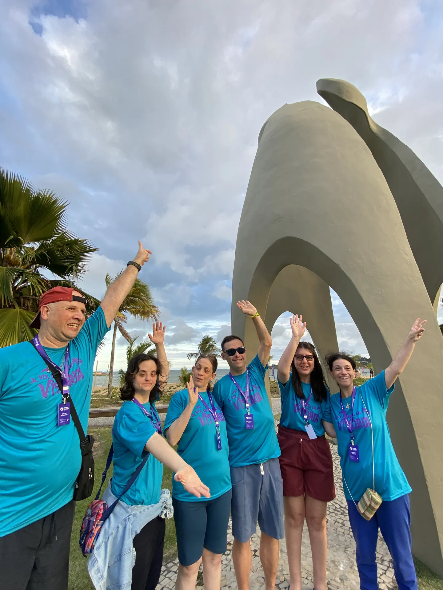 Participantes acenam em frente a um monumento à beira-mar.