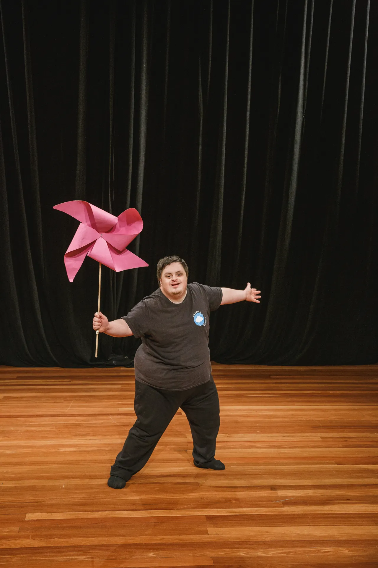 Atriz sozinha no palco segura um cata-vento rosa.