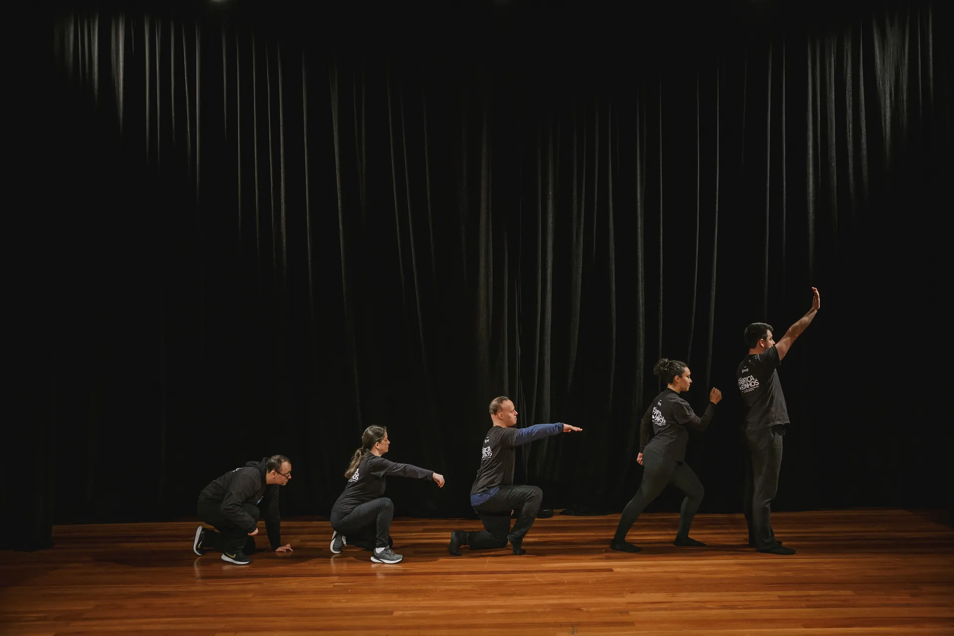 Atores espalhados pelo palco durante uma cena do espetáculo.