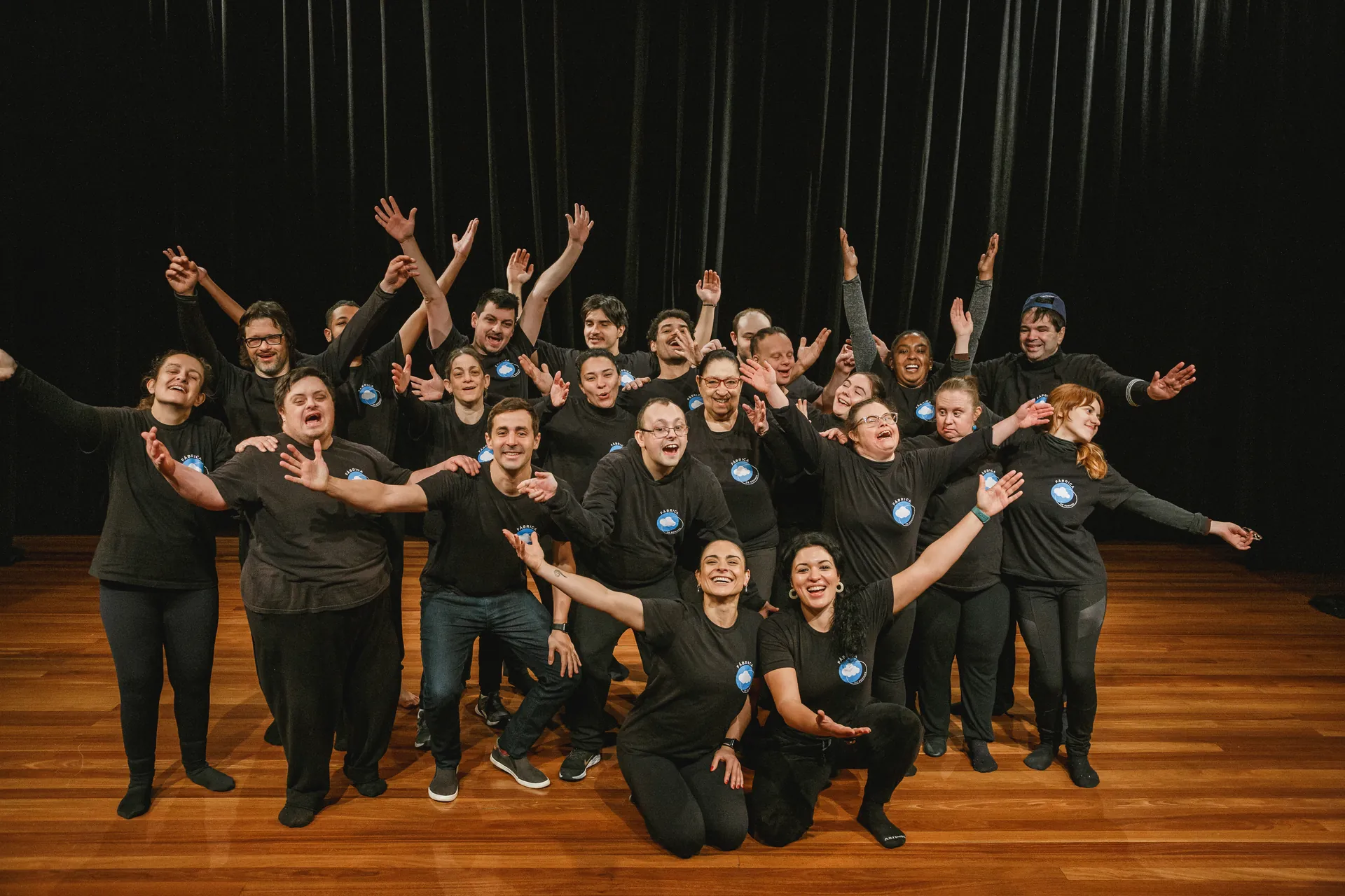 Elenco da Fábrica de Sonhos reunido no palco, de braços abertos.