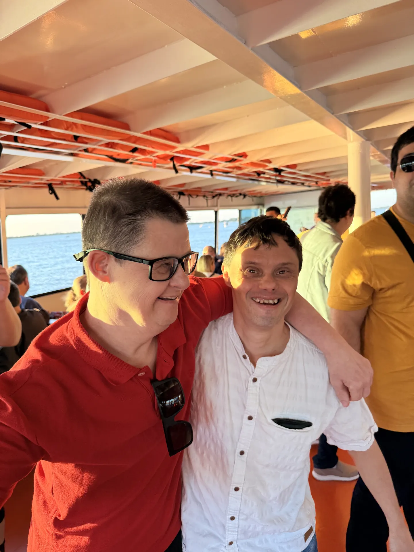 Dois participantes abraçados no deck de um barco, sorrindo para a câmera.