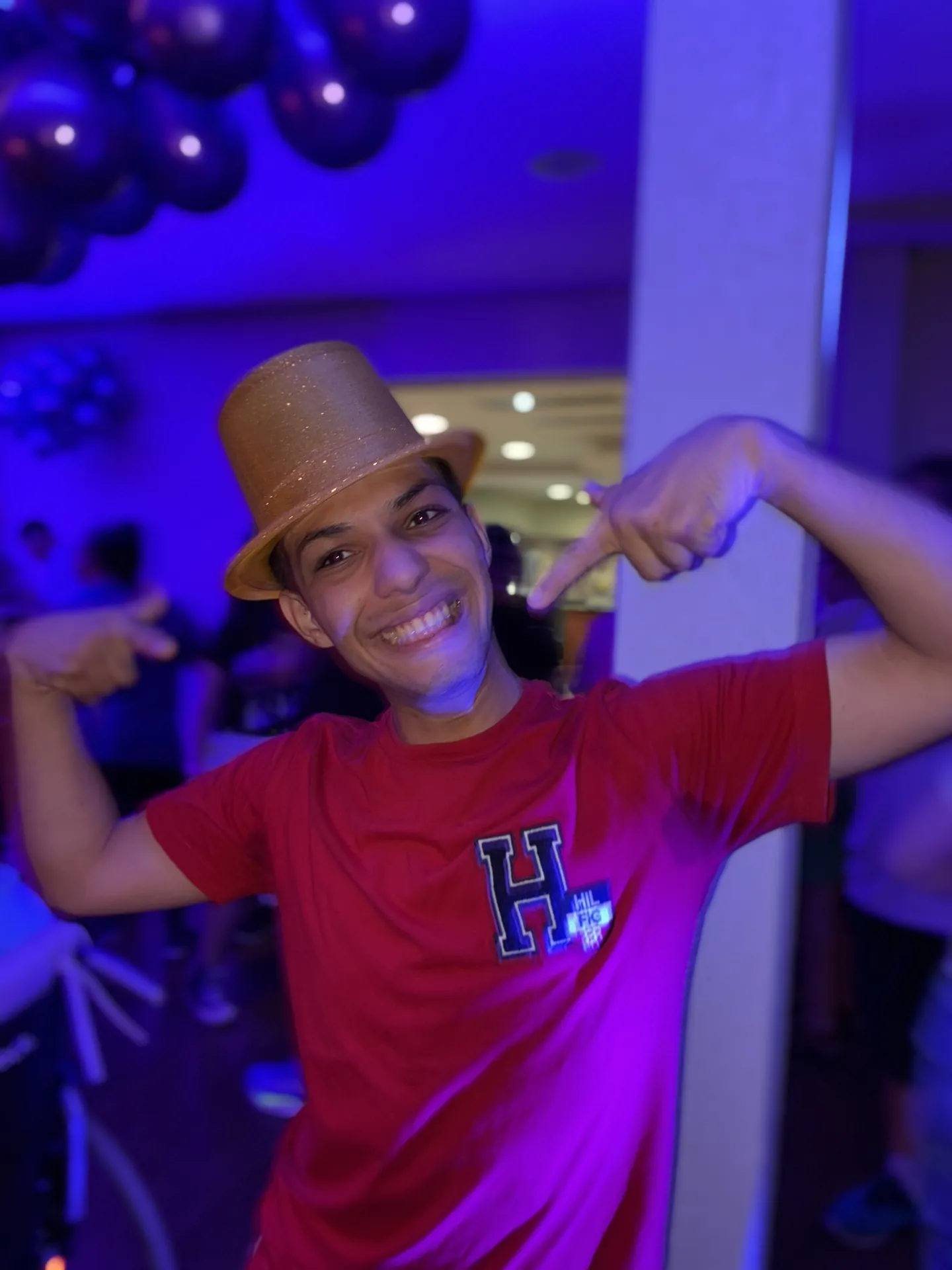 Participante de cartola dourada posa numa festa iluminada.