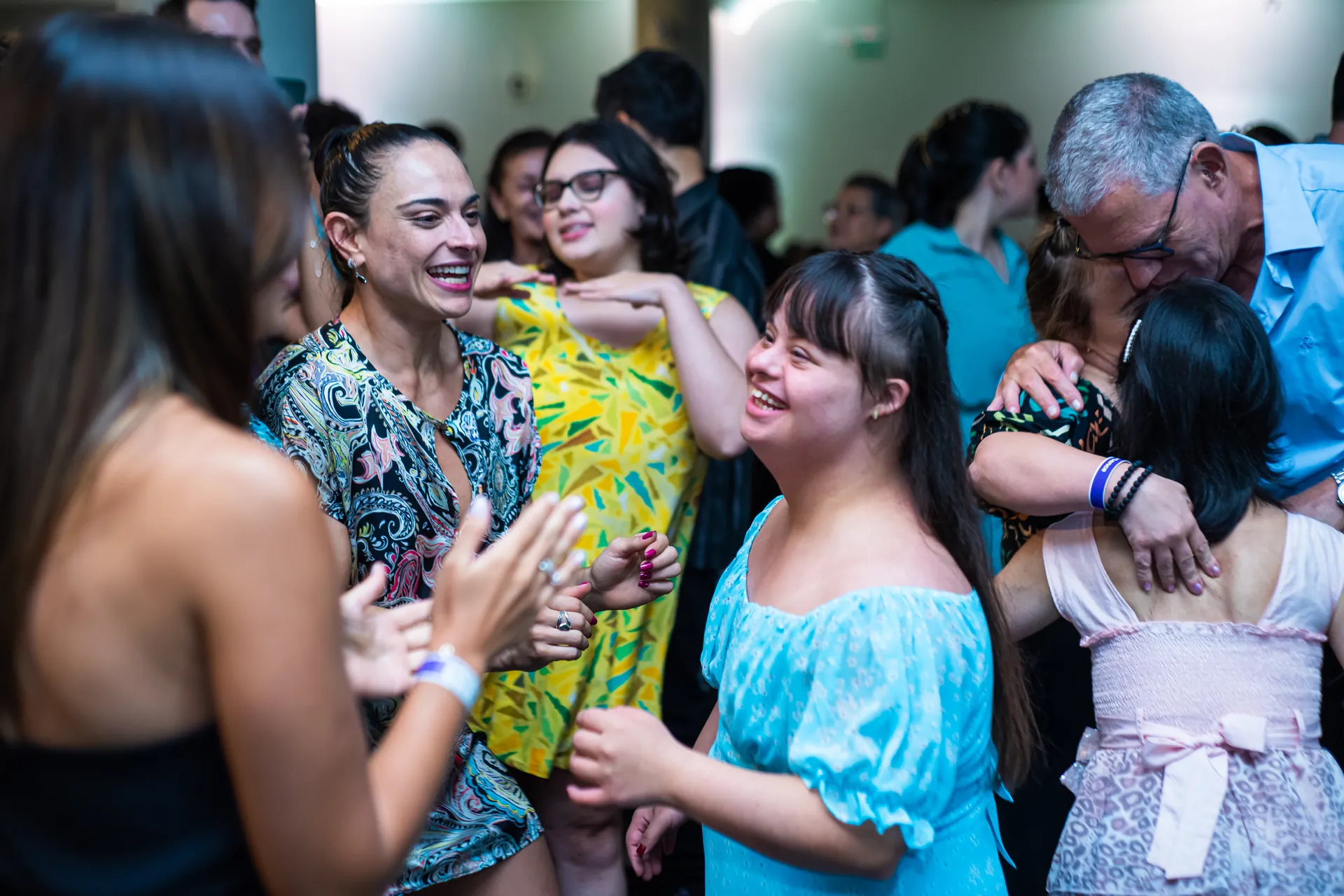Participantes dançam juntos numa festa, com roupas coloridas.