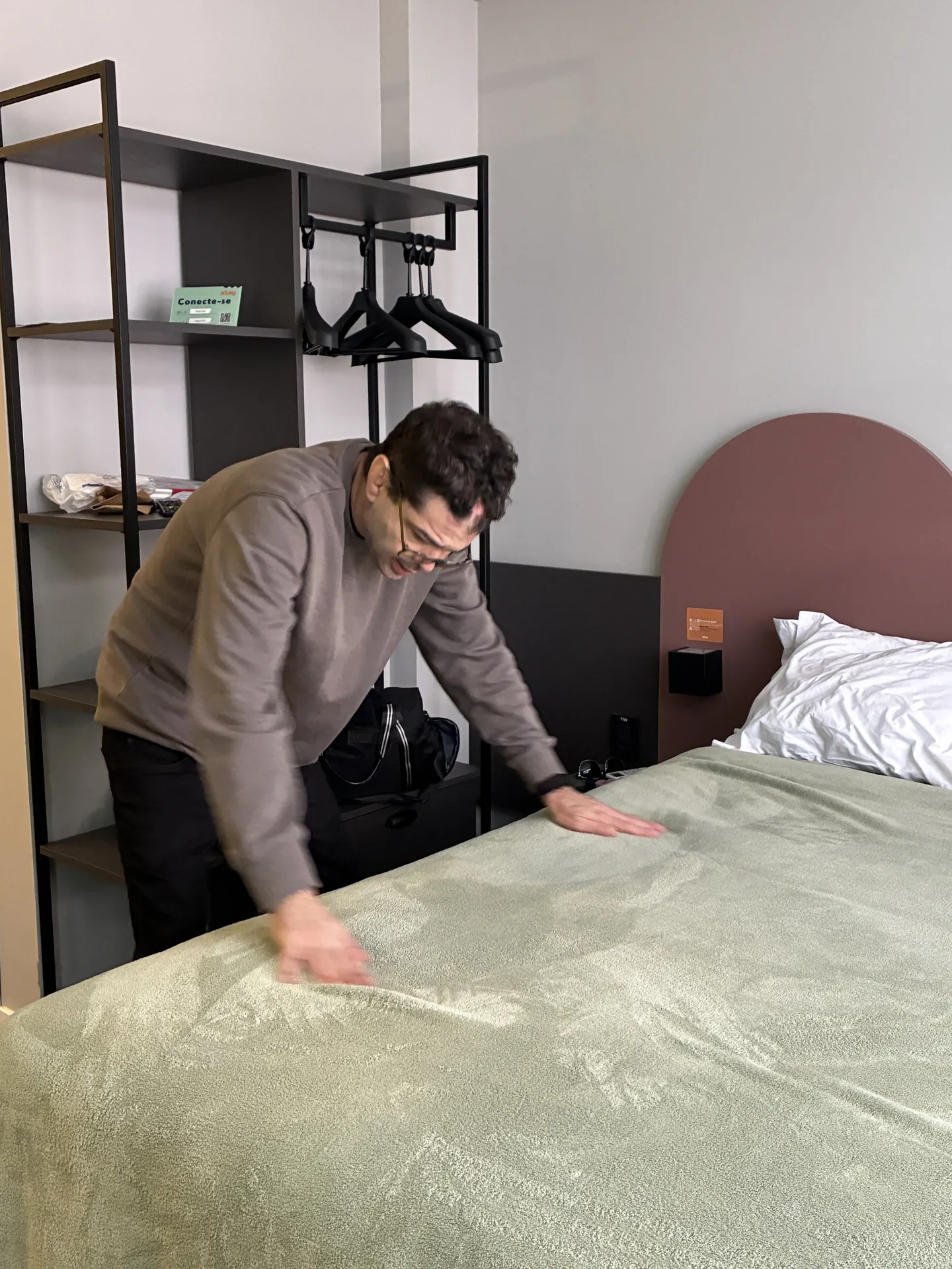 Participante estica o lençol para arrumar a cama do quarto de hotel.