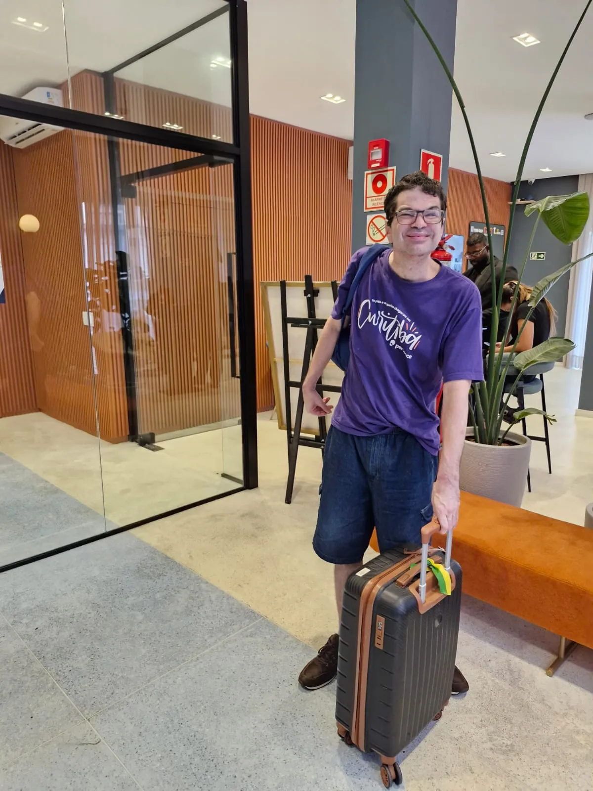 Participante chega ao hotel puxando a própria mala, sorrindo.