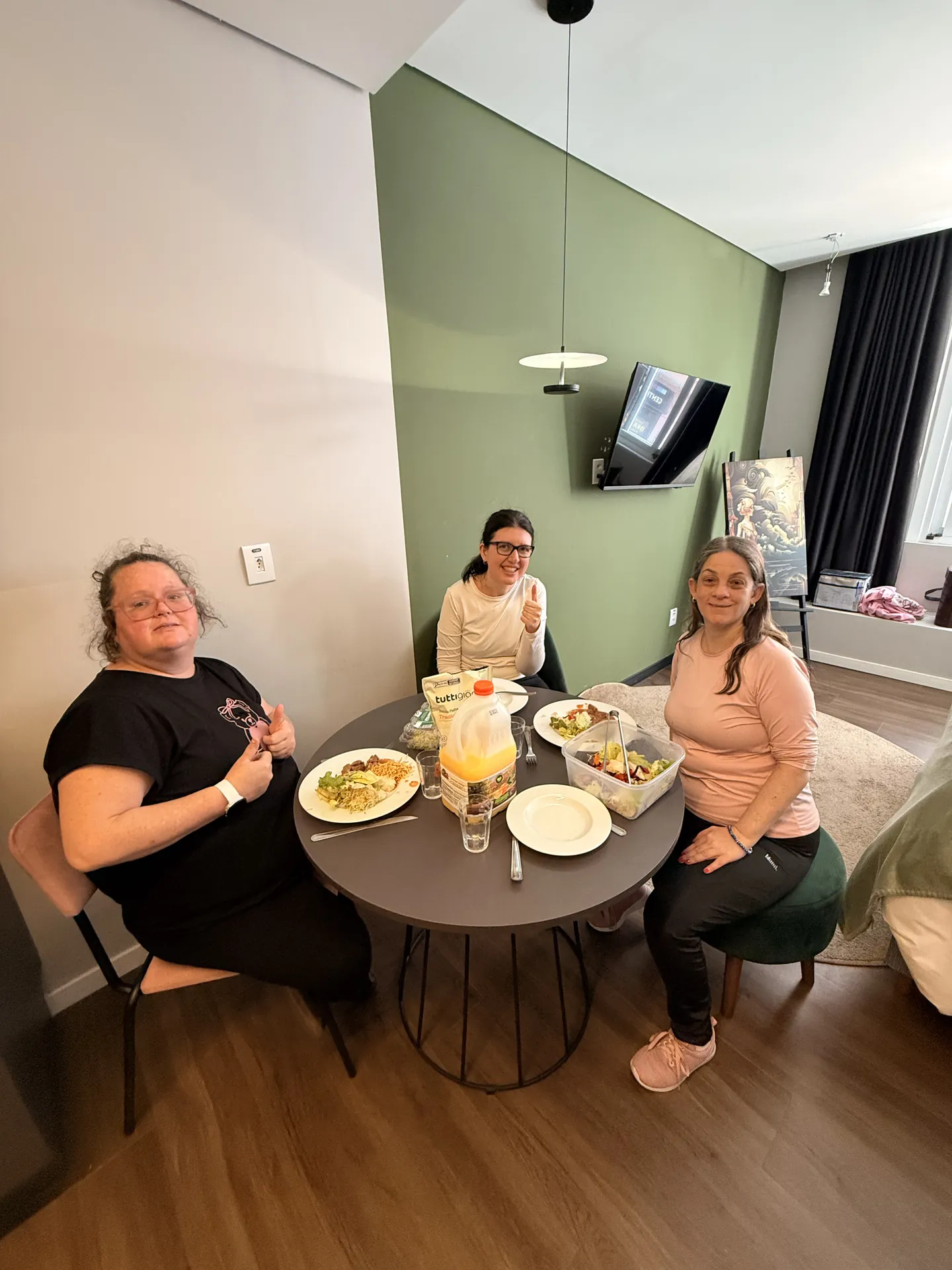 Três participantes fazem uma refeição juntas na mesa do quarto.