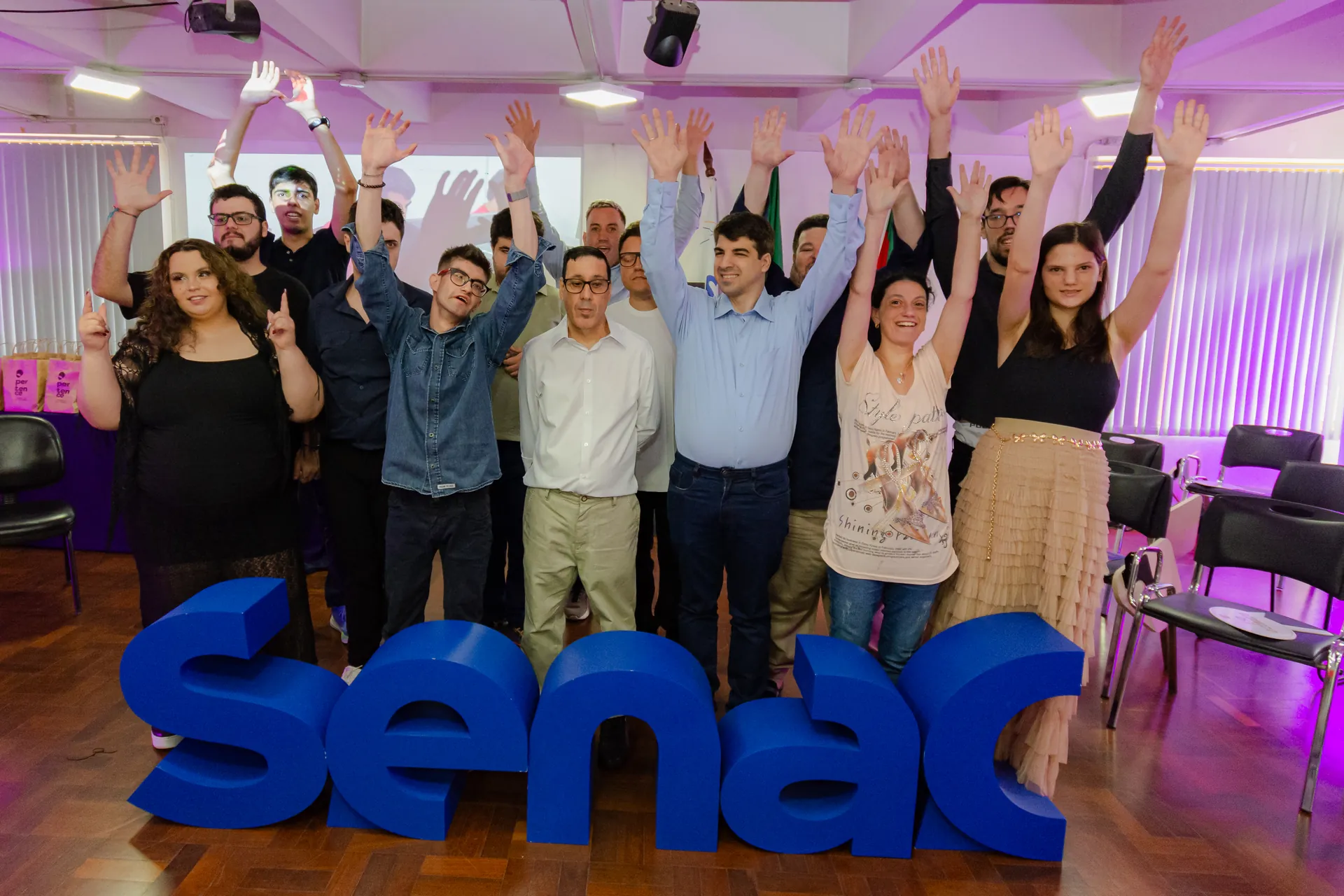 Grupo comemora de braços erguidos junto ao letreiro do SENAC.