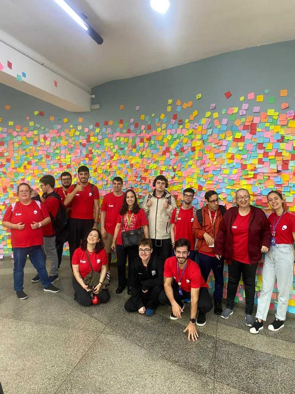 Turma posa diante de um painel coberto de post-its coloridos.