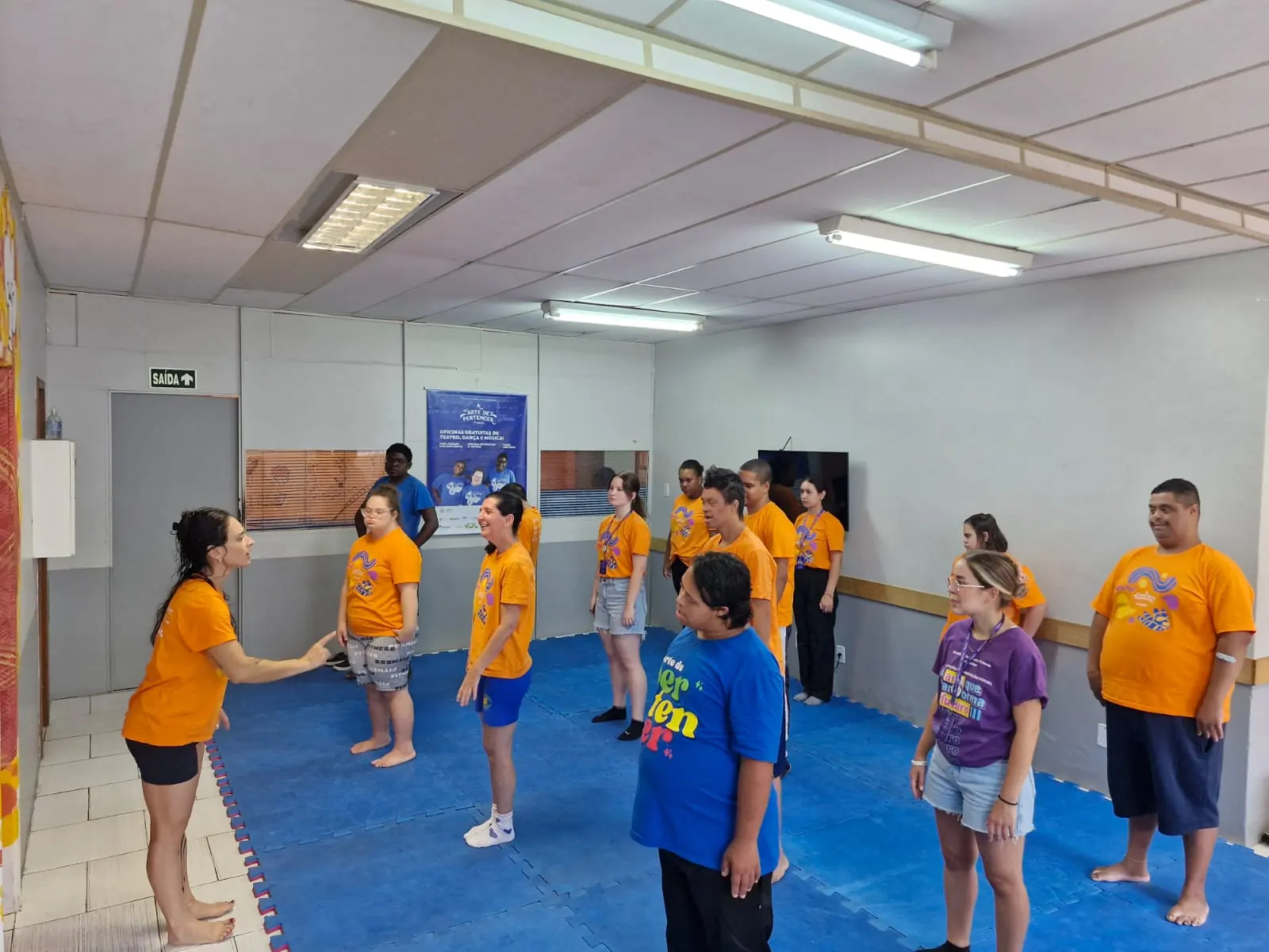 Turma da oficina de dança espalhada pela sala de ensaio.