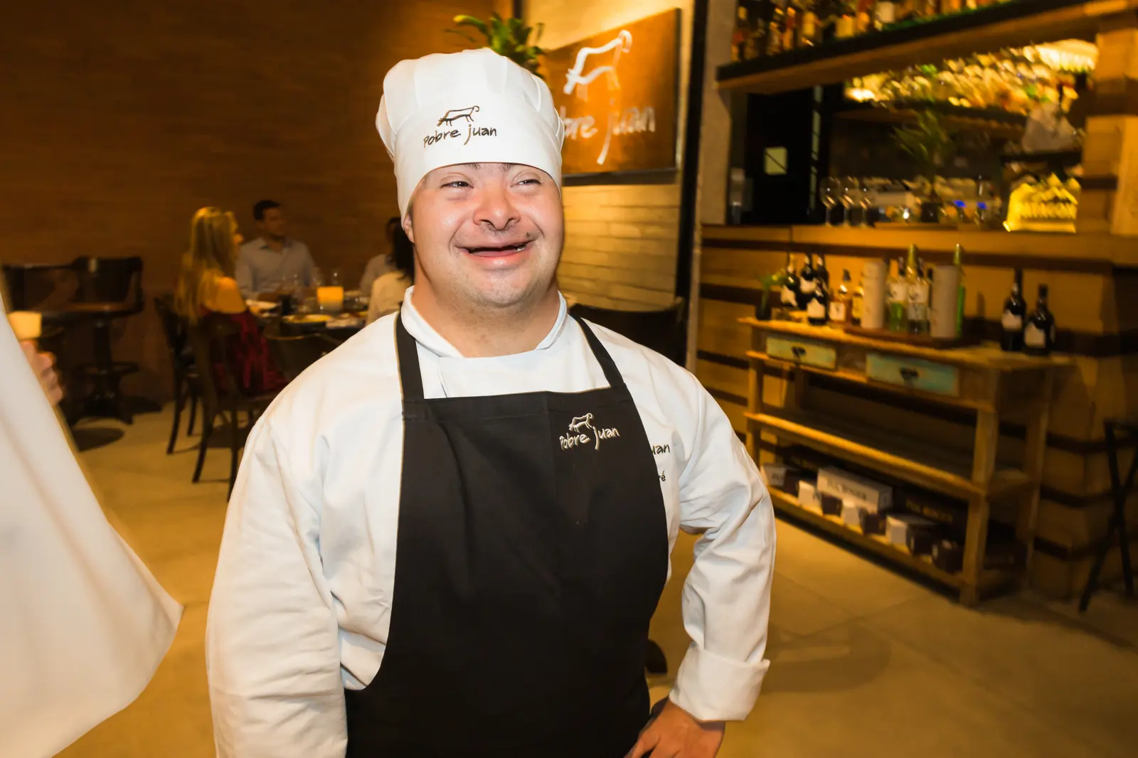 Participante de dólmã e touca de chef posa no salão do restaurante.