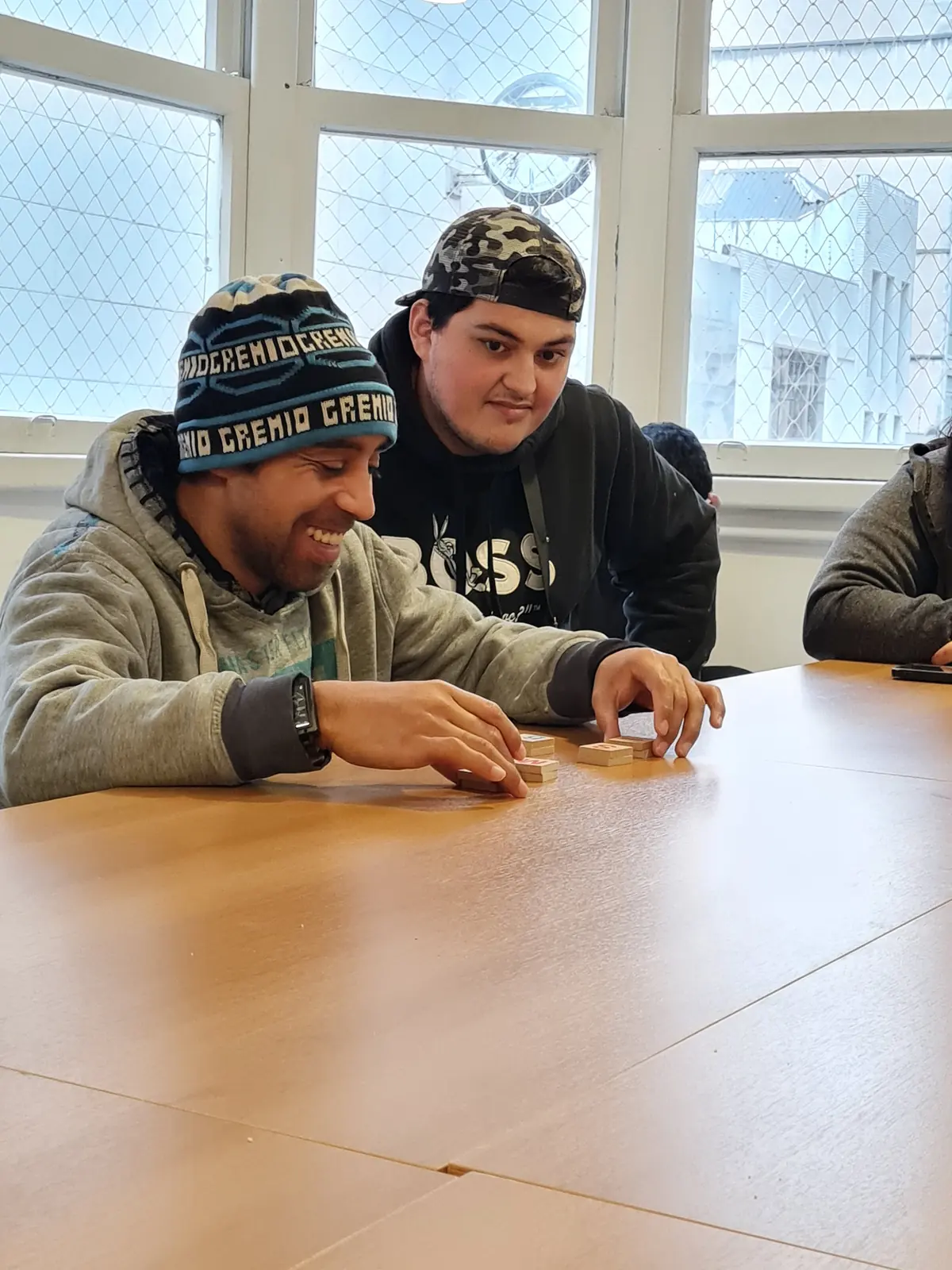 Dois participantes montam palavras com peças de letras sobre a mesa; um deles sorri.