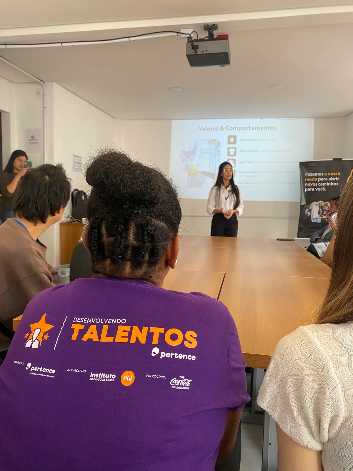 Participantes assistem à apresentação de uma profissional de empresa parceira; em primeiro plano, a camiseta do Desenvolvendo Talentos.