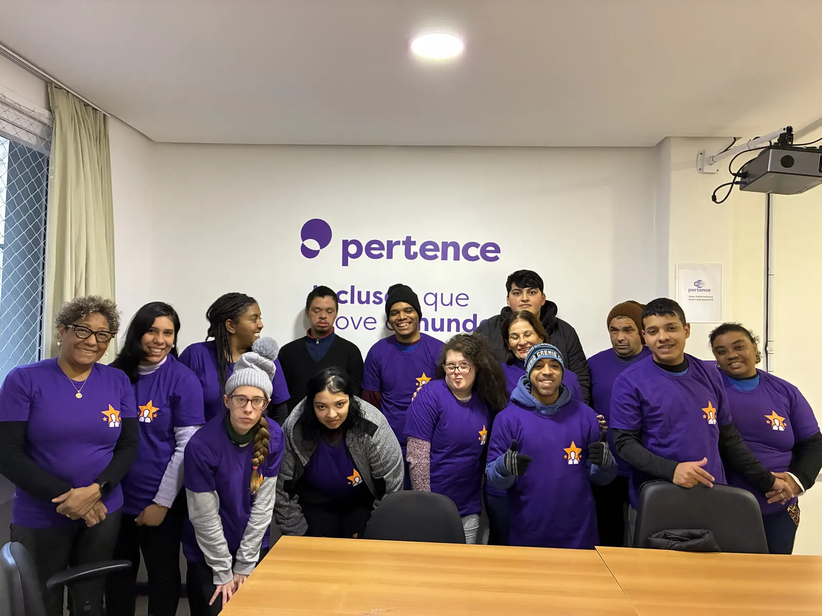 Turma do Desenvolvendo Talentos posa de camiseta roxa do projeto diante da parede com a marca Pertence.