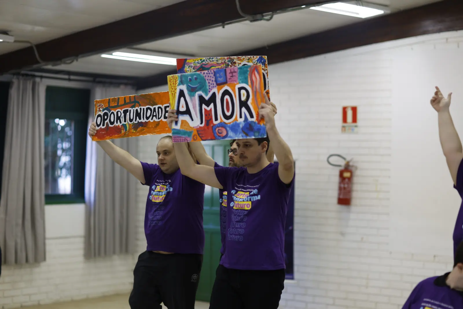 Dois participantes seguram cartazes com as palavras oportunidade e amor.