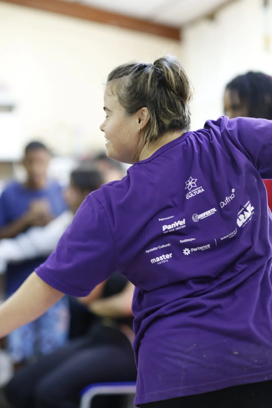 Participante de camiseta roxa com o braço erguido na oficina de dança.