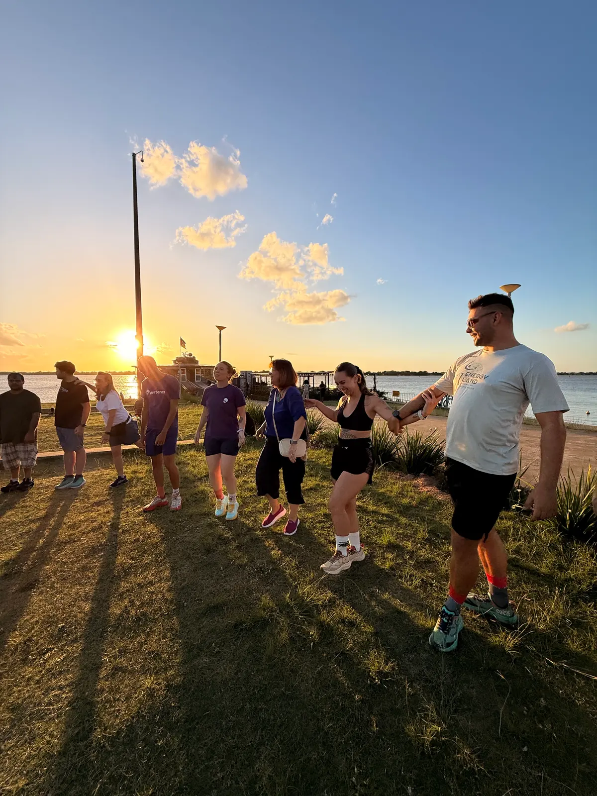 Participantes de mãos dadas durante o alongamento ao pôr do sol.