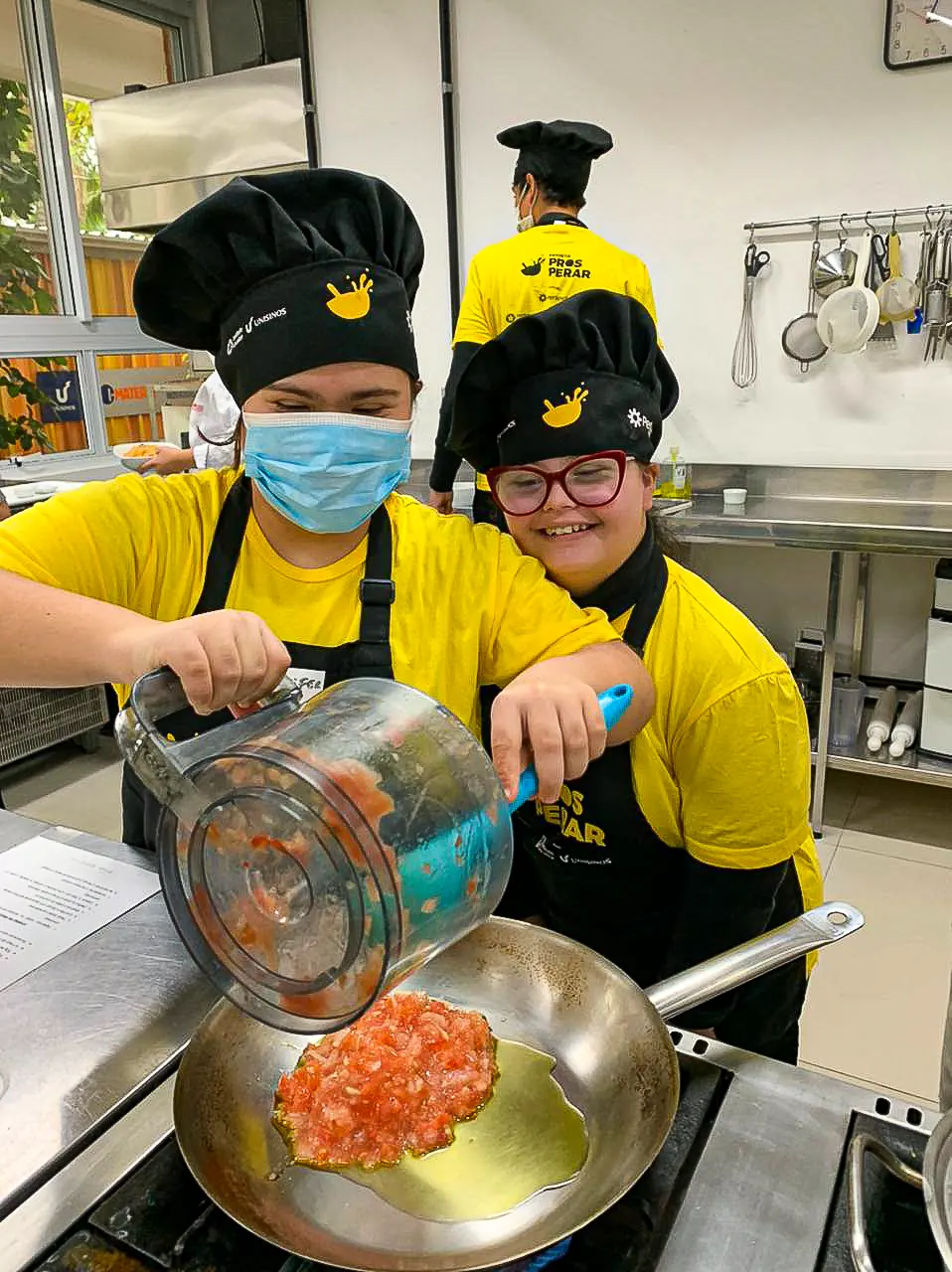 Dupla de participantes prepara uma receita na bancada da cozinha.