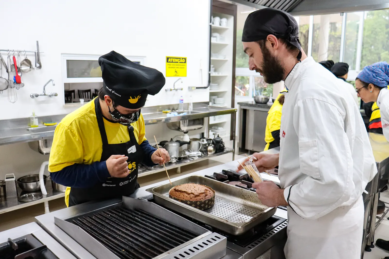Participante prepara um corte na grelha ao lado do chef instrutor.