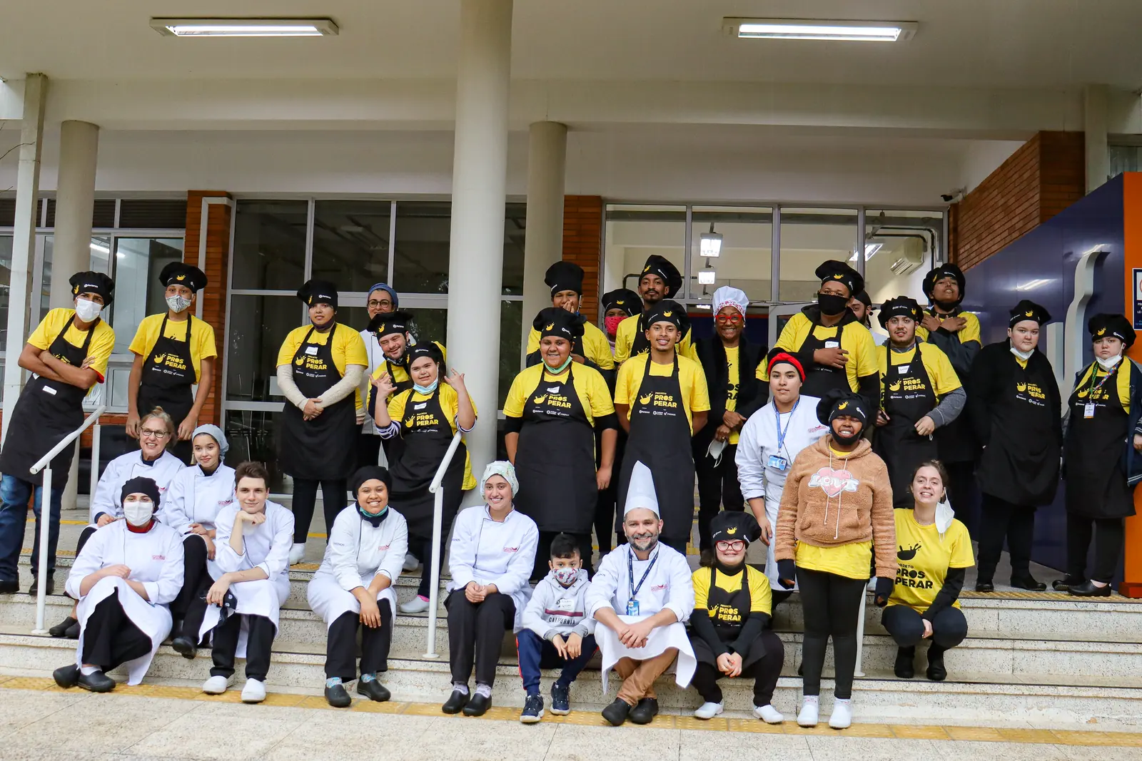 Turma do projeto reunida na escada da escola de gastronomia, de uniforme.